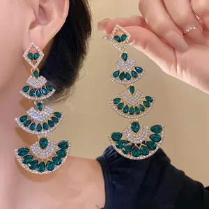 Detailed close-up of luxury fan-shaped dangle earrings with green teardrop crystals