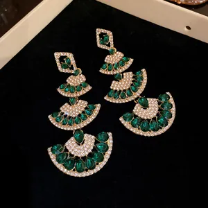 Macro detail of emerald green fan-shaped drop earrings with sparkling rhinestone accents.