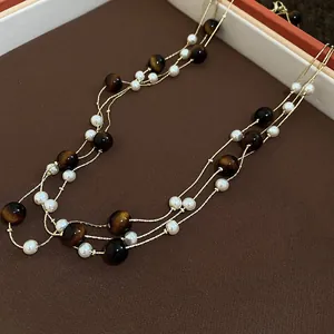 Dettaglio di perle occhio di tigre e perle bianche su una collana d'oro a più fili