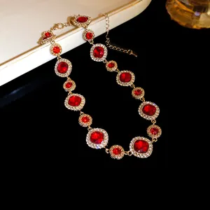 Dettaglio di collana dorata con grandi cristalli rossi tondi e accenti di diamanti.