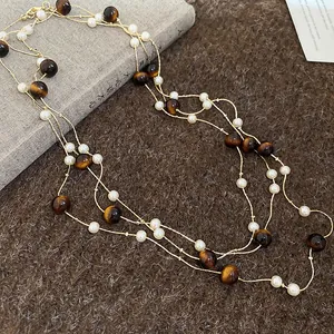 Primo piano di collana a più strati con perle occhio di tigre marroni e perle bianche su catena oro.