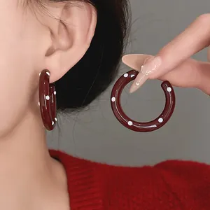 Detail view of burgundy enamel hoop earrings with white polka dots worn by a model