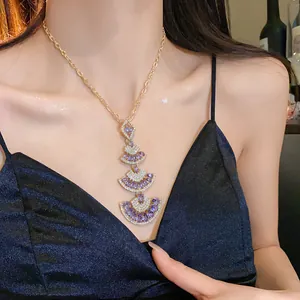 Detailed view of a gold fan-shaped pendant necklace with purple stones on a model