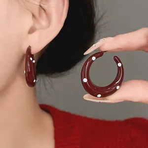 Close-up detail of vintage style red enamel polka dot hoop earrings on an Asian model