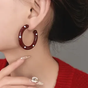 Detail shot of retro burgundy enamel hoop earrings with white polka dots worn by model