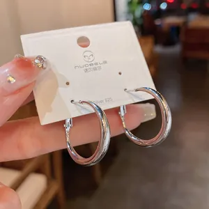 Detalle de pendientes de aro minimalistas plateados brillantes en tarjeta blanca
