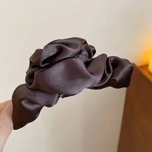 Dettaglio ravvicinato di una lussuosa clip per capelli in raso marrone scuro tenuta in mano.