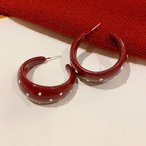 Detailed close-up of retro dark red enamel C-shaped hoop earrings with white polka dot pattern
