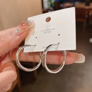 Primer plano de pendientes de aro plateados minimalistas en un soporte de tarjeta de marca