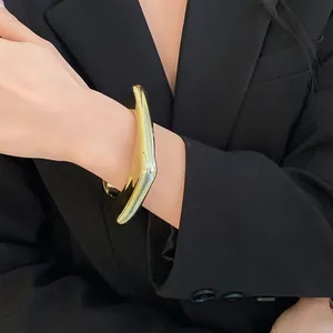 Détail de gros bracelet jonc géométrique irrégulier doré sur bras avec blazer noir