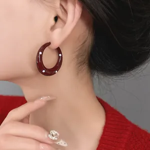 Detail showing a retro burgundy enamel hoop earring with white polka dots on ear
