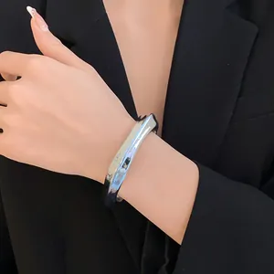 Gros plan d'un bracelet ouvert argenté géométrique irrégulier porté au poignet d'un mannequin.