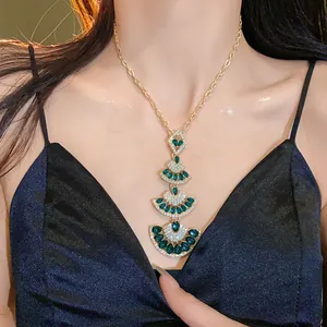 Close-up of a luxury gold fan-shaped tiered pendant necklace with green stones.