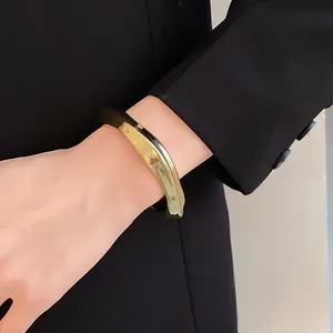 Gros plan d'un bracelet jonc géométrique irrégulier doré porté sur un poignet en blazer.