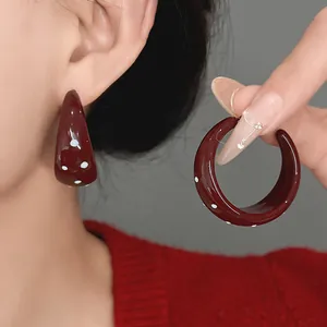 Close-up view showing the glossy burgundy C-shaped earrings with retro white polka dot pattern