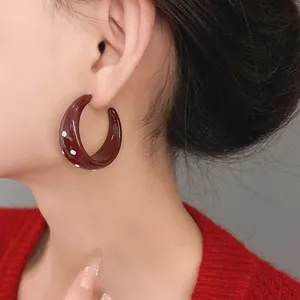 Close-up view of vintage burgundy polka dot C-shaped hoop earrings worn by model