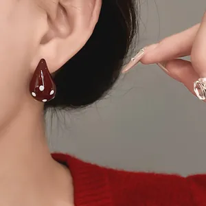 Close-up of vintage burgundy enamel teardrop stud earrings with white polka dots