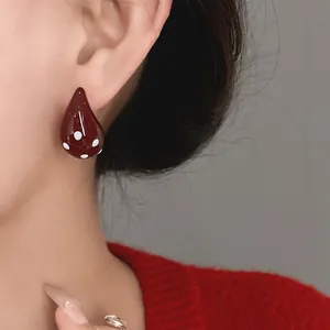 Close-up of vintage red teardrop enamel stud earrings featuring white polka dots on model