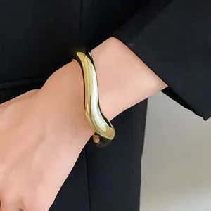 Gros plan d'un bracelet jonc ouvert doré irrégulier minimaliste porté au poignet.