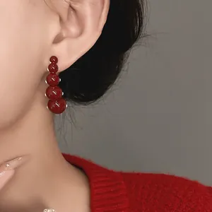 Detailed view of glossy dark red beaded drop earrings worn by a model in red sweater