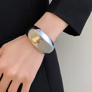 Gros plan d'un bracelet ouvert argenté minimaliste au poignet avec un blazer noir.