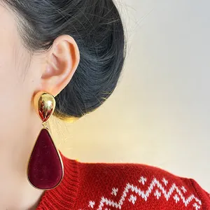Macro view of retro teardrop earrings featuring dark red velvet and gold metal on model