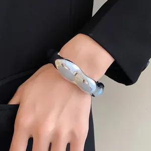 Détail d'un bracelet jonc argenté irrégulier porté au poignet avec un blazer noir.