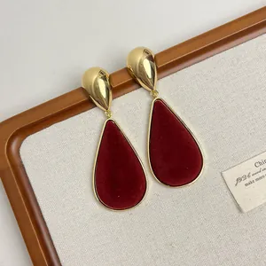 Detail shot of elegant vintage teardrop earrings featuring dark red velvet and gold plating.