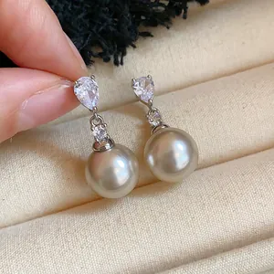 Macro view of teardrop zircon and round pearl drop earrings on beige velvet