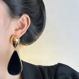 Detailed view of elegant black velvet teardrop earring with golden trim on model's ear.