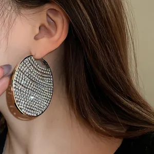 Close-up detail of large silver metal hoop earrings with sparkling zircon stones.