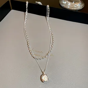 Macro detail of a double-layered necklace with a water-drop pearl pendant.