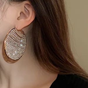 Close-up of oversized gold-toned hoop earrings with sparkling pavé zircon stones on a model.