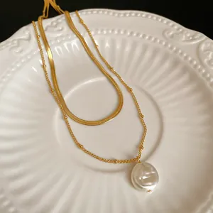 Macro detail of a double-layered gold necklace with a white baroque pearl pendant