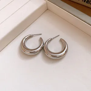 Detailed view of silver chunky C-shaped hoop earrings on a textured display tray