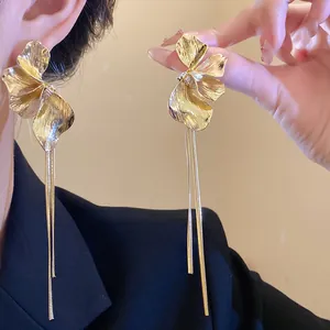 Close-up detail of large gold flower stud earrings with long elegant metallic tassels