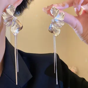 Close-up detail of silver flower tassel earrings worn on ear and held by hand