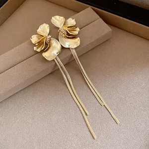 Close-up detail of golden flower tassel earrings with textured petals on a brown display.