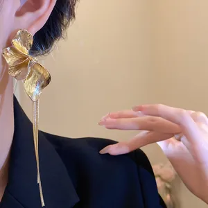 Elegant gold floral tassel earrings with long metallic chains shown on a model's ear