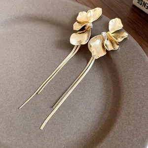 Close-up of gold flower tassel earrings with intricate petal texture on a brown plate