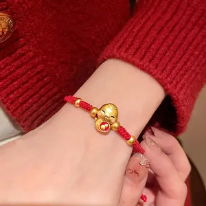 Gros plan détaillé d'un bracelet festif en corde tressée rouge avec un charm serpent doré.