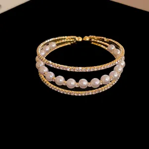 Detailed close-up of a three-layered gold cuff bracelet with pearls and rhinestones.