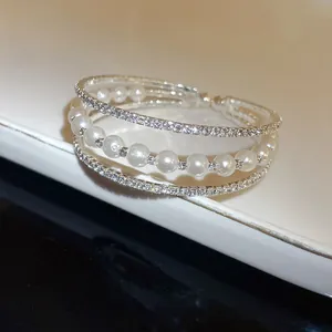 Detailed close-up of a three-layer silver bracelet featuring rhinestones and white pearls