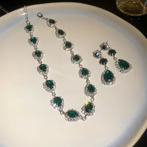 Detailed view of elegant emerald green teardrop necklace and earring set on a white plate.