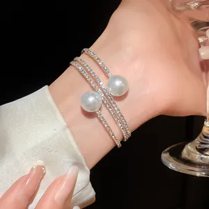 Close-up of elegant triple-layer rhinestone bracelet with two white pearls on wrist.