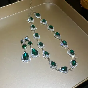 Close-up of sparkling emerald green water drop necklace and earring set on gold tray