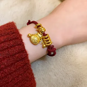 Gros plan détaillé d'un bracelet en corde rouge avec des breloques dorées.