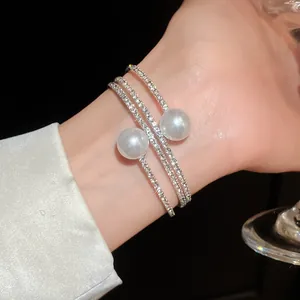Macro view of a luxury three-layer open bangle with rhinestones and white pearls on wrist