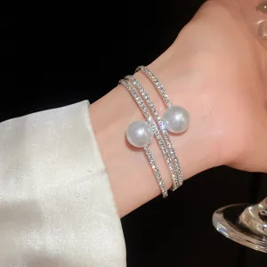 Close-up of elegant triple-layered silver bangle featuring two pearls and rhinestones.
