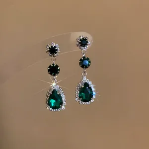 Detailed view of elegant emerald green teardrop rhinestone dangling earrings with starburst.